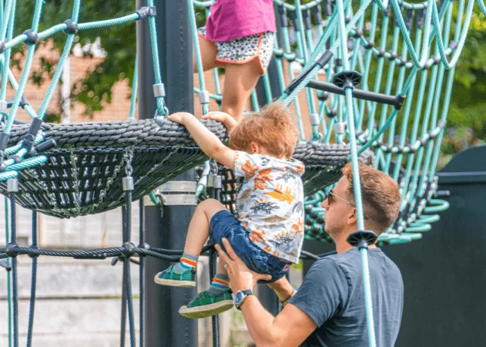 Parent Supervising Children On Playground Swings For Safety