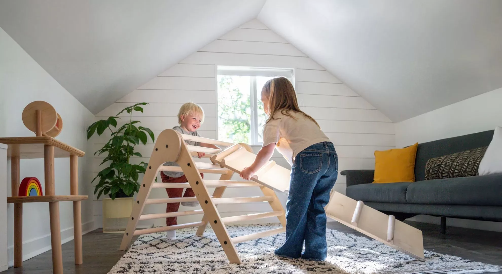 Toddler independently climbing wooden Montessori triangle climber in natural lit playroom, open ended learning environment